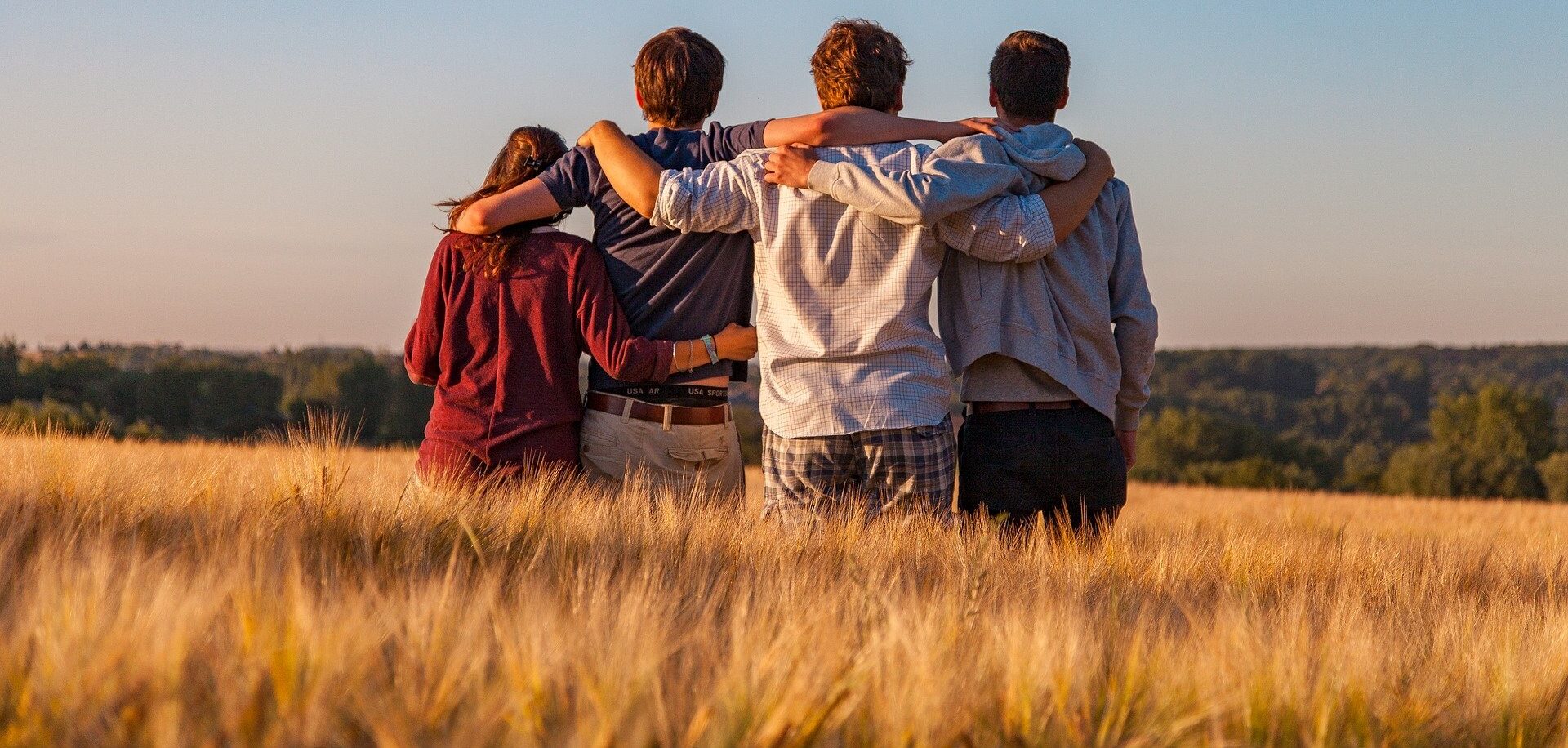 vier stehen mit dem Rücken zum Betrachter Jugendliche stehen in einem Gerstenfeld, die Arme umeinander gelegt